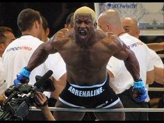 a man with no shirt on standing in front of a camera and wearing boxing gloves