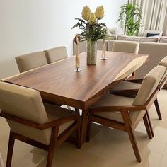 a wooden table surrounded by beige chairs and vase with flowers on it in a living room