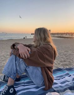 a woman sitting on top of a blanket at the beach