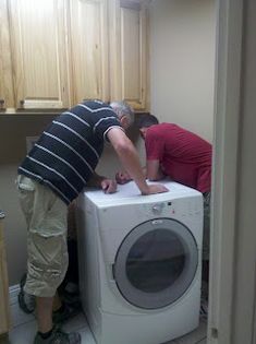 two men are doing something on top of a washing machine while another man stands over the washer