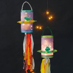 two colorful lights hanging from strings on a black background, one has a frog and the other is a fish