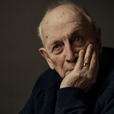 an older man with his hand on his chin looking at the camera while wearing a black sweater