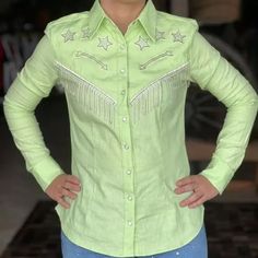 a woman standing with her hands on her hips wearing a green shirt and blue jeans