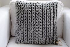 a gray knitted pillow sitting on top of a white couch