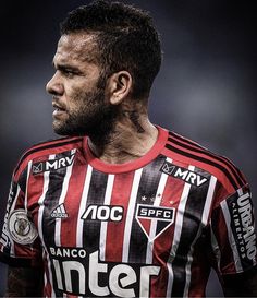 a soccer player in a red and black uniform looking off to the side with his head tilted