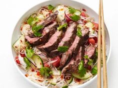 a white bowl filled with meat and veggies next to two chopsticks