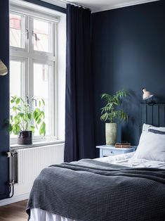 a bedroom with dark blue walls and white bedding, potted plants on the nightstand