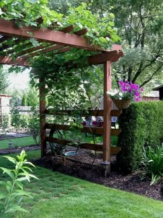 a garden area with green grass, plants and a wooden pergoline structure in the middle