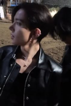 a woman with black hair wearing a leather jacket and ear piercings standing next to another person