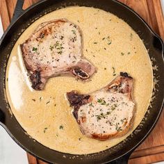 two pork chops cooking in a skillet on top of a wooden cutting board