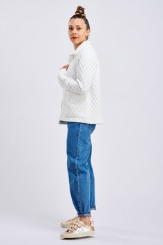 a woman in white sweater and jeans standing with her hand on her hip, looking off to the side