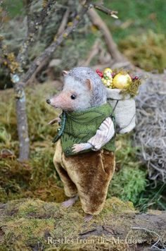 a stuffed animal rat carrying some fruit on its back in the woods with trees and grass behind it