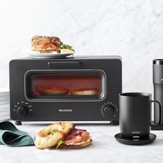 a toaster oven sitting on top of a counter next to a coffee mug and sandwich