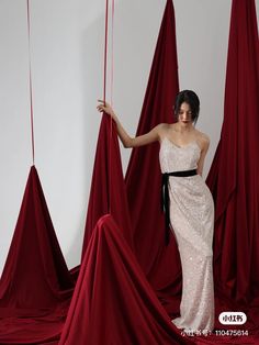 a woman standing in front of red drapes with her hands on the strings,