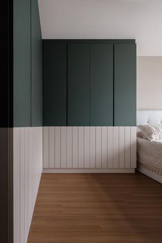 an empty bedroom with green cabinets and white sheets on the bed, along with wood flooring