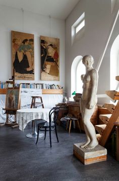 a statue is standing in the middle of a room with paintings on the walls and stairs