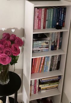 a vase filled with pink roses sitting on top of a table next to a book shelf