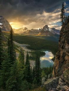 the sun is setting over a mountain lake and trees in the foreground, with mountains in the background