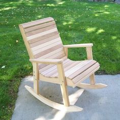 a wooden rocking chair sitting on top of a cement slab in front of green grass