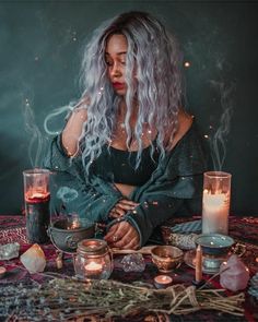 a woman sitting at a table with candles in front of her and surrounded by other items