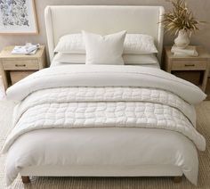 a bed with white linens and pillows in a small room next to two nightstands