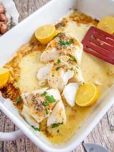 an oven baked fish dish with lemons and parsley on top, in a white casserole dish