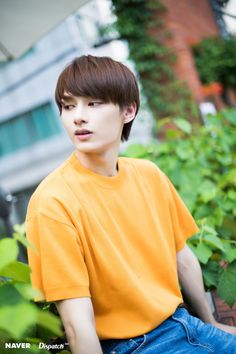 a young man sitting on top of a wooden bench next to green plants and trees