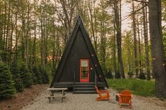 a small cabin in the woods with two orange chairs