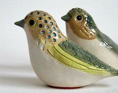 two ceramic birds sitting side by side on a white surface with one bird looking at the other