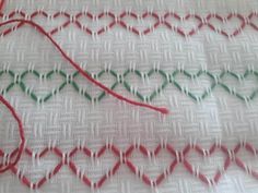 some red and green thread is on the white fabric with two different colored lines that are connected to each other