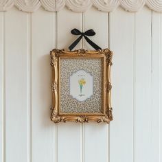 a gold frame hanging on the wall with a black bow around it's neck