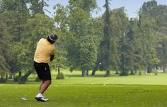 a man is swinging his golf club at the green on a sunny day with trees in the background