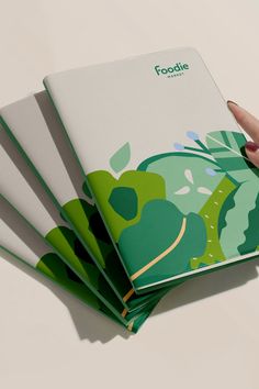 a hand is holding an open book with green leaves on the front and back cover