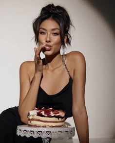 a woman sitting in front of a cake on top of a white plate and holding her hand to her mouth