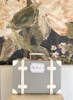 a suitcase sitting on top of a wooden table in front of a wall with flowers