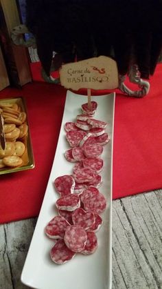 several slices of salami on a white platter next to some crackers and other snacks