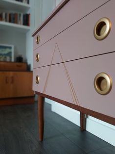 a pink dresser with gold knobs in a living room next to a bookshelf