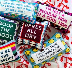 embroidered pillows with sayings on them sitting on a tablecloth covered surface in various colors and patterns