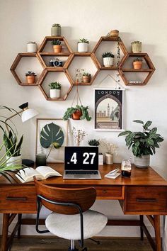 a desk with a laptop on top of it and some potted plants in the corner