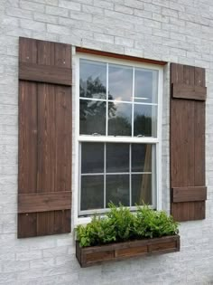 an open window with wooden shutters and green plants in the window box below it