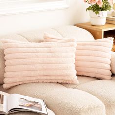 the pillows are stacked on top of each other in front of a book and vase with flowers