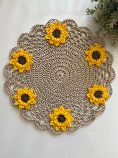 crocheted doily with yellow sunflowers on white surface next to plant