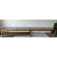 a wooden bench sitting on top of a cement floor next to a white brick wall