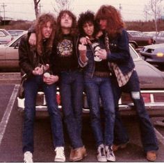 four young men sitting on the back of a pickup truck in a parking lot with their arms around each other