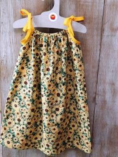 a sunflower print dress hanging on a wooden wall with a hanger attached to it