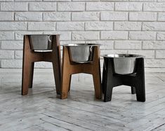 three metal bowls sitting on top of wooden stools in front of a brick wall