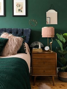 a bedroom with green walls and two pictures on the wall above the bed, next to a nightstand with a lamp