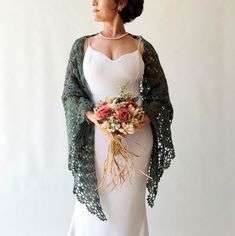 a woman in a white dress and green shawl with flowers on her chest holding a bouquet