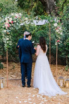 the bride and groom are standing under an outdoor wedding ceremony arch with flowers on it