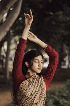 a woman in a sari is doing yoga exercises on the street with her hands up